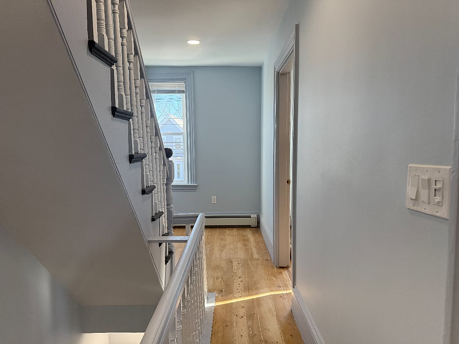 Hallway with doors to bathroom, second floor bedroom, kitchen, and stairs leading up. On the other end of the hallway is a space to put a desk. 