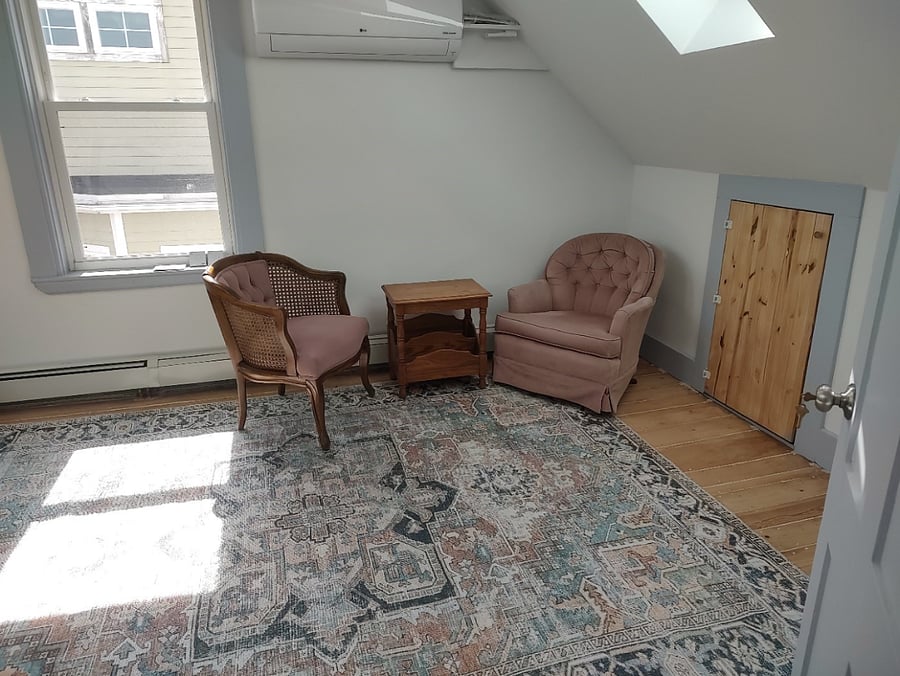 Bedroom on third floor. One side of the room has two sitting chairs and small table. 