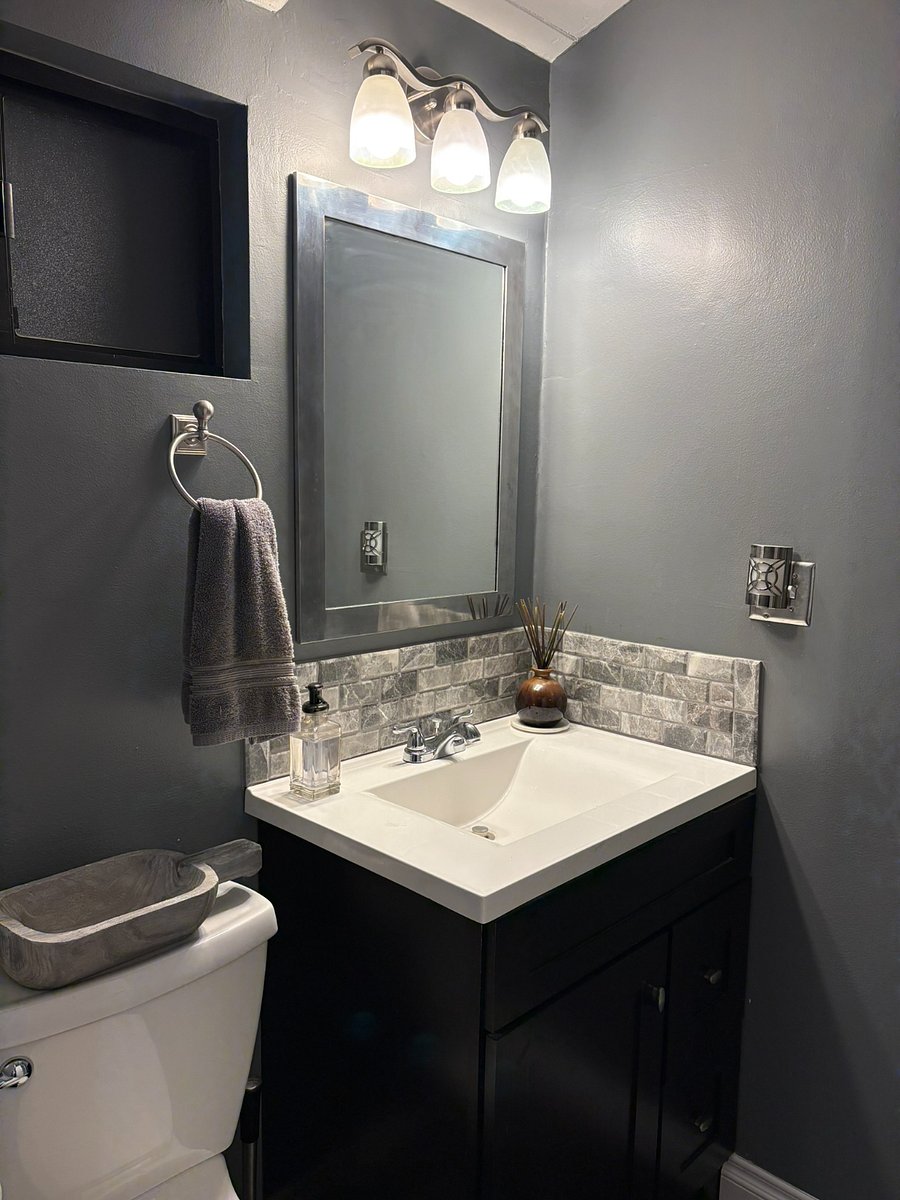 The second bathroom has dark walls, stone tile backsplash and brushed nickel fixtures giving this bathroom a boutique hotel feel.