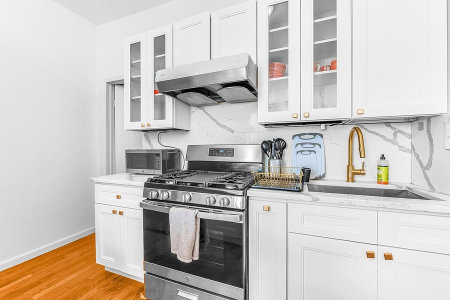 Renovated white kitchen with gas range, hood, and glass-front cabinets.