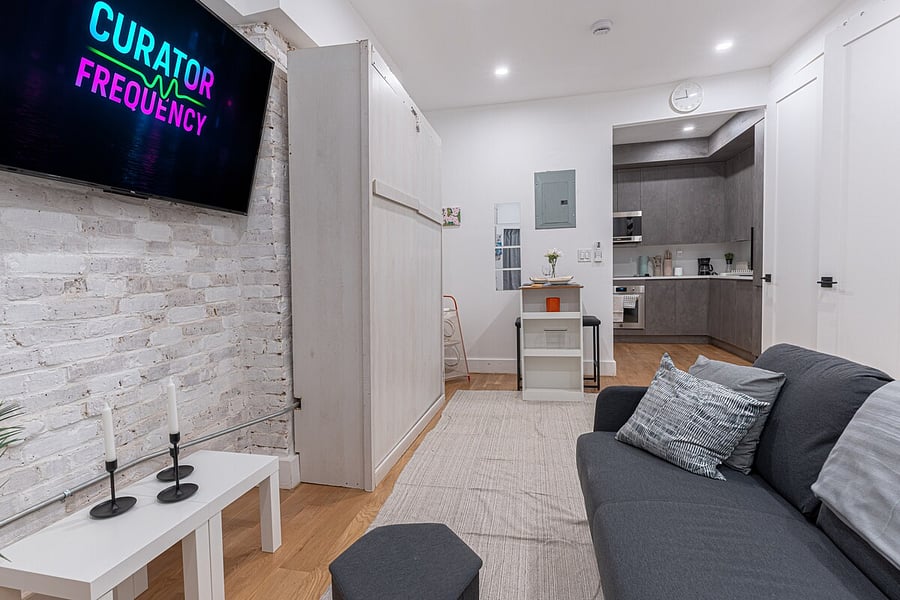 Cozy living space with smart TV, comfy seating and exposed brick, opening to the kitchen  a warm, modern Brooklyn hideaway.