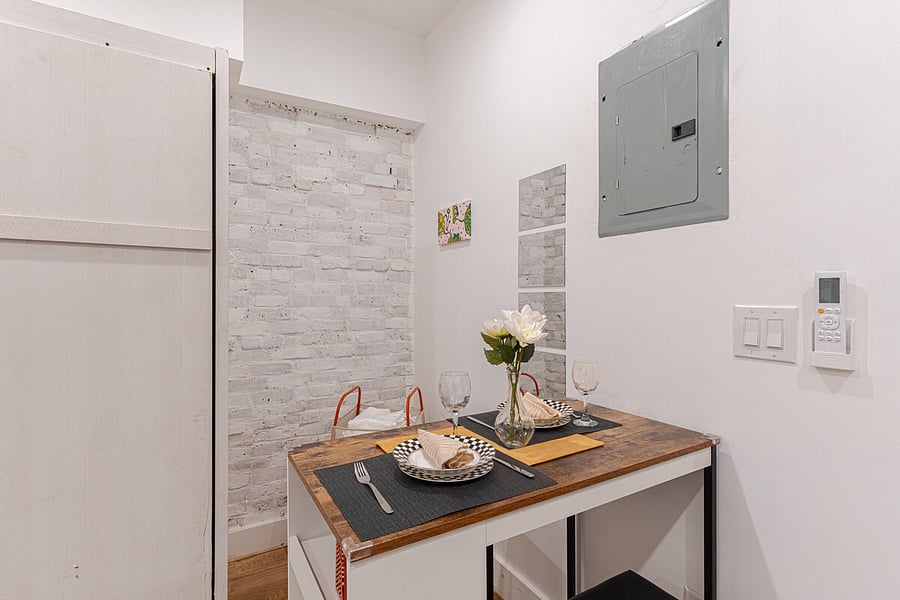 Smart studio layout with a comfortable bed against an exposed-brick wall, opening to a sleek modern kitchen.