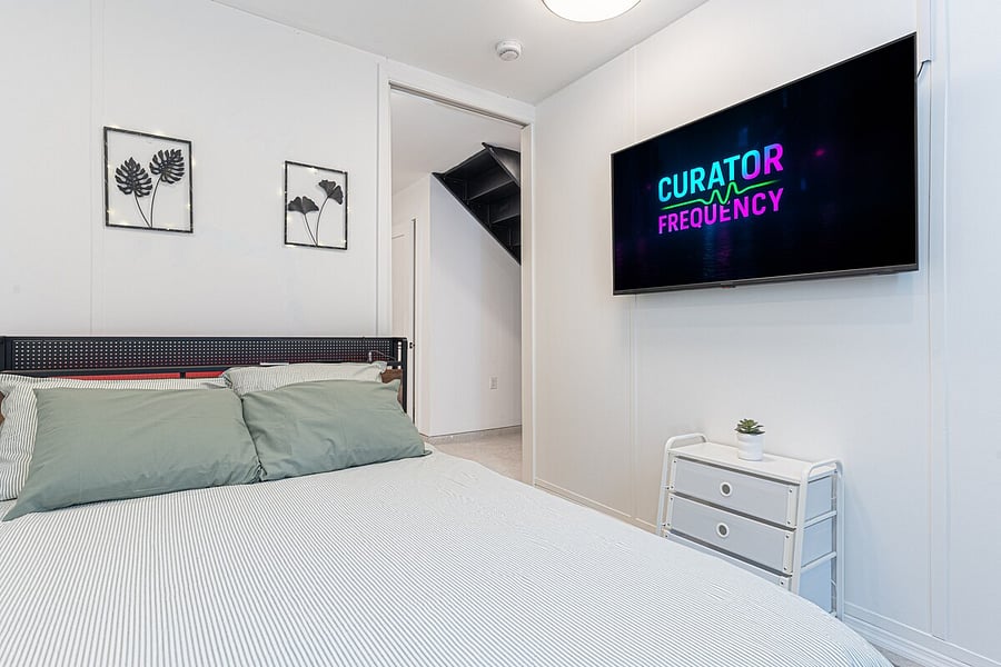 Lower-level bedroom by the staircase with a comfy bed, dresser, and TV  the duplex's second sleep space.