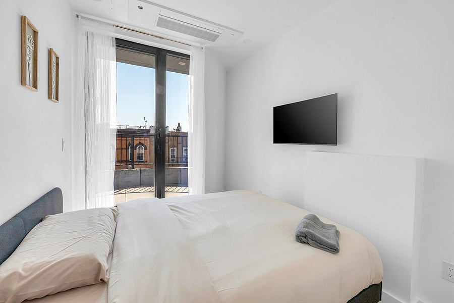 Bright bedroom with crisp white linens, a wall-mounted TV and big windows.