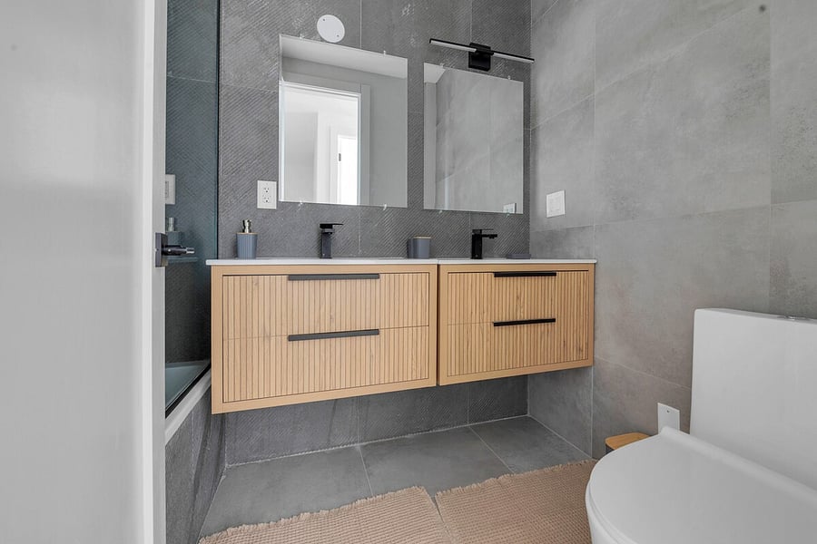 Sleek bathroom with a double wood vanity, wide mirror and modern fixtures.