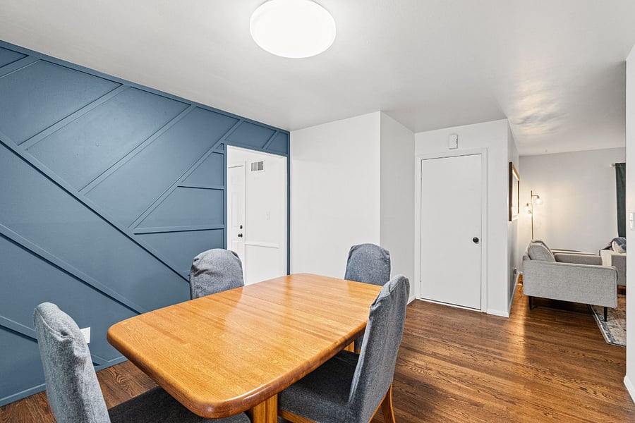 Dining room. A real table for real meals, seating six. A gold framed mirror and accent wall, with doors that open the room to natural light. After a long travel day, this is where everyone lands.