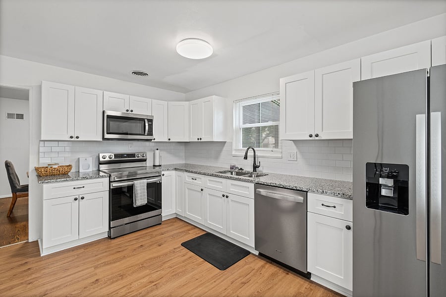 A kitchen you will actually use for 30 days. Granite counters, a full stainless steel appliance set including a dishwasher, white shaker cabinets, and a subway tile backsplash. This is what a fully equipped kitchen really looks like.