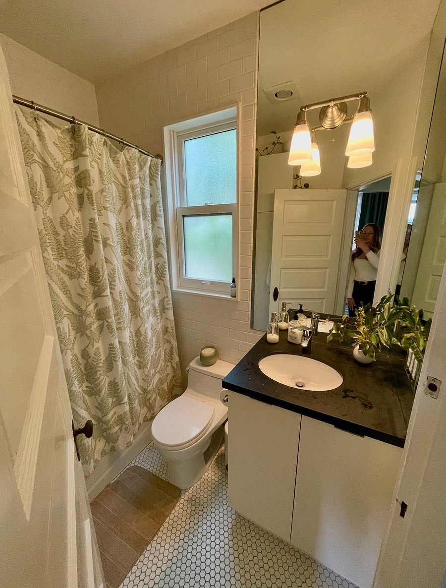 The bathroom is also upstairs, and it has been redone with white subway tile. There is under the sink storage and cabinet storage. The window is frosted for privacy, but a bamboo stand behind the window gives added greenery too.