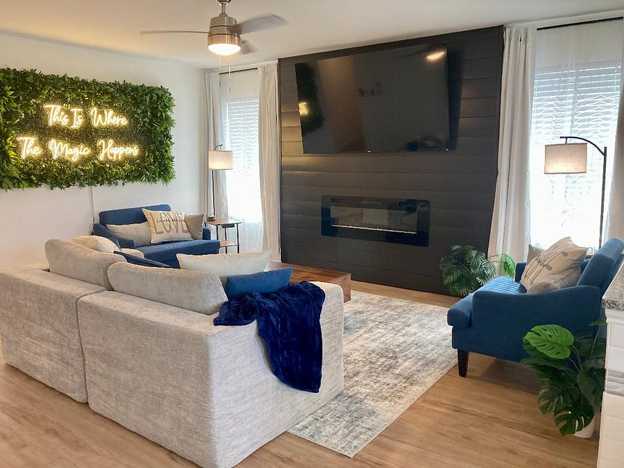 Living room with boneless loveseat and two over-sized single chairs flanking a large accent wall with electric fireplace and 75" 4K UHD Roku TV.