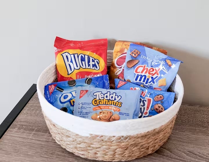 A clean, welcoming snack setup featuring a curated basket of individually wrapped treats, perfect for a quick bite or late-night craving.