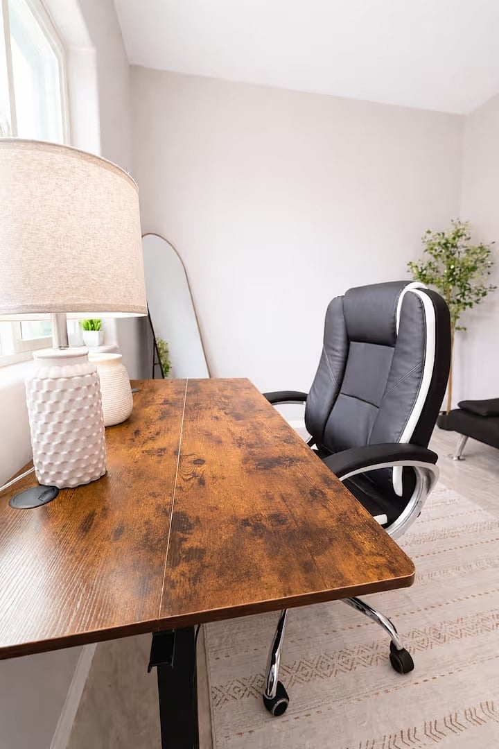 A quiet, well-lit workspace featuring a large wood desk, comfortable executive chair, and calming dcor, ideal for remote work or study.