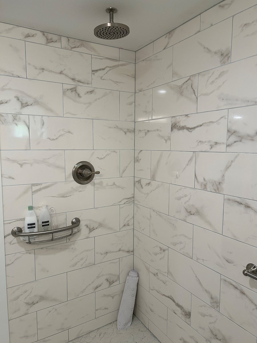 There is a rain shower with handrails and soap/shampoo holder next to the shower handle.