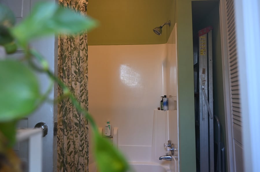 Green bathroom has backyard view, bath and shower. 