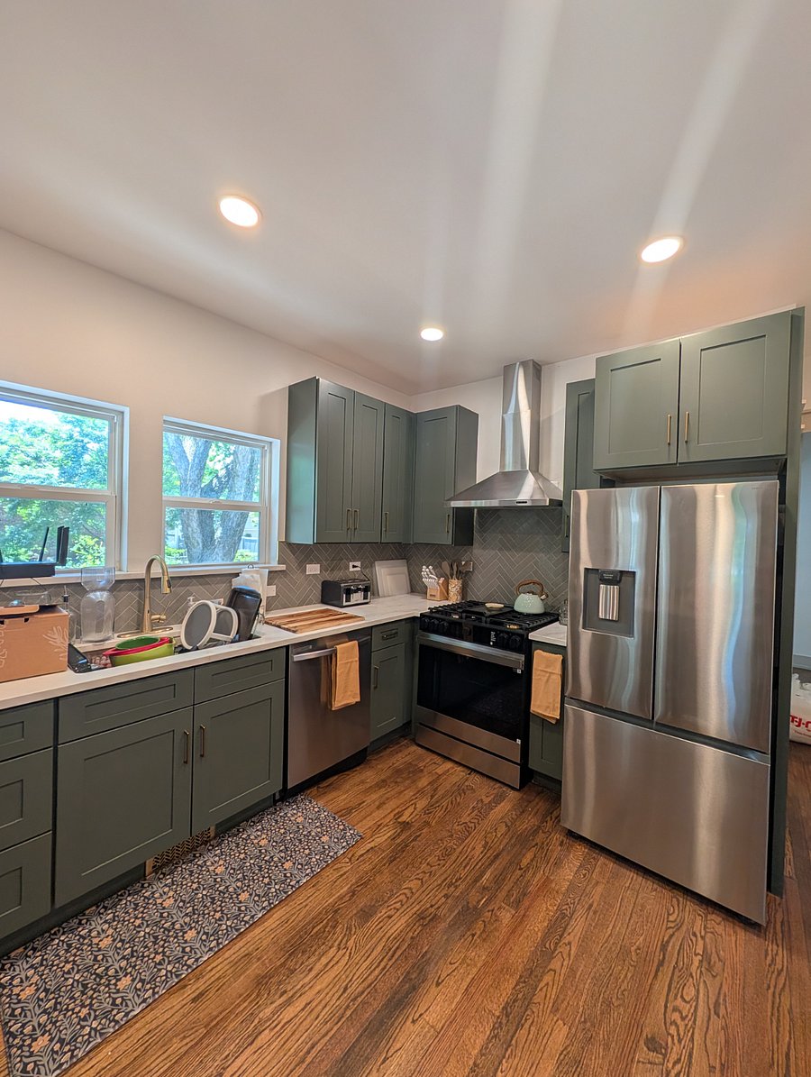 Chef's kitchen featuring sage-green shaker cabinets, quartz countertops, gas range, stainless appliances, and herringbone tile backsplash.