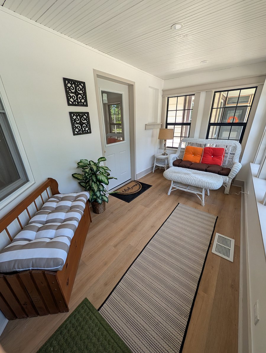 Enclosed sunroom with wicker loveseat, ottoman, bench seating, and plenty of natural light.