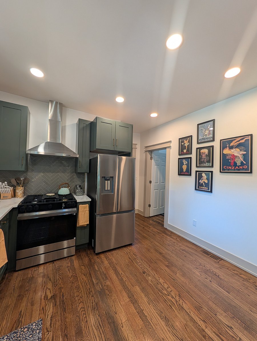 Chef's kitchen featuring sage-green shaker cabinets, quartz countertops, gas range, stainless appliances, and herringbone tile backsplash.