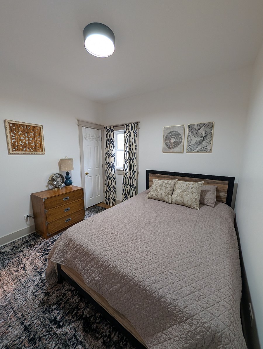 Bedroom with quilted bedding, campaign dresser, patterned curtains, and area rug.