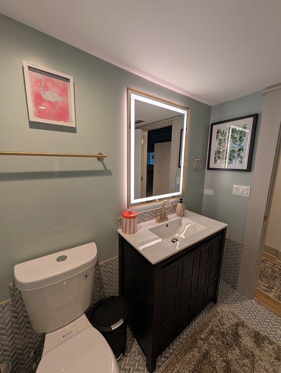 Bathroom with backlit vanity mirror, dark wood vanity, and single-sink ceramic top.