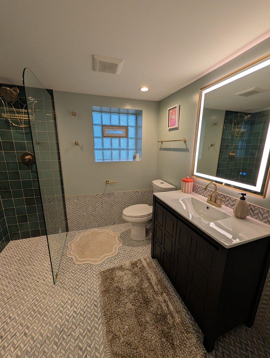 Full bathroom with emerald-tile walk-in shower, glass partition, marble mosaic floors, and gold fixtures.