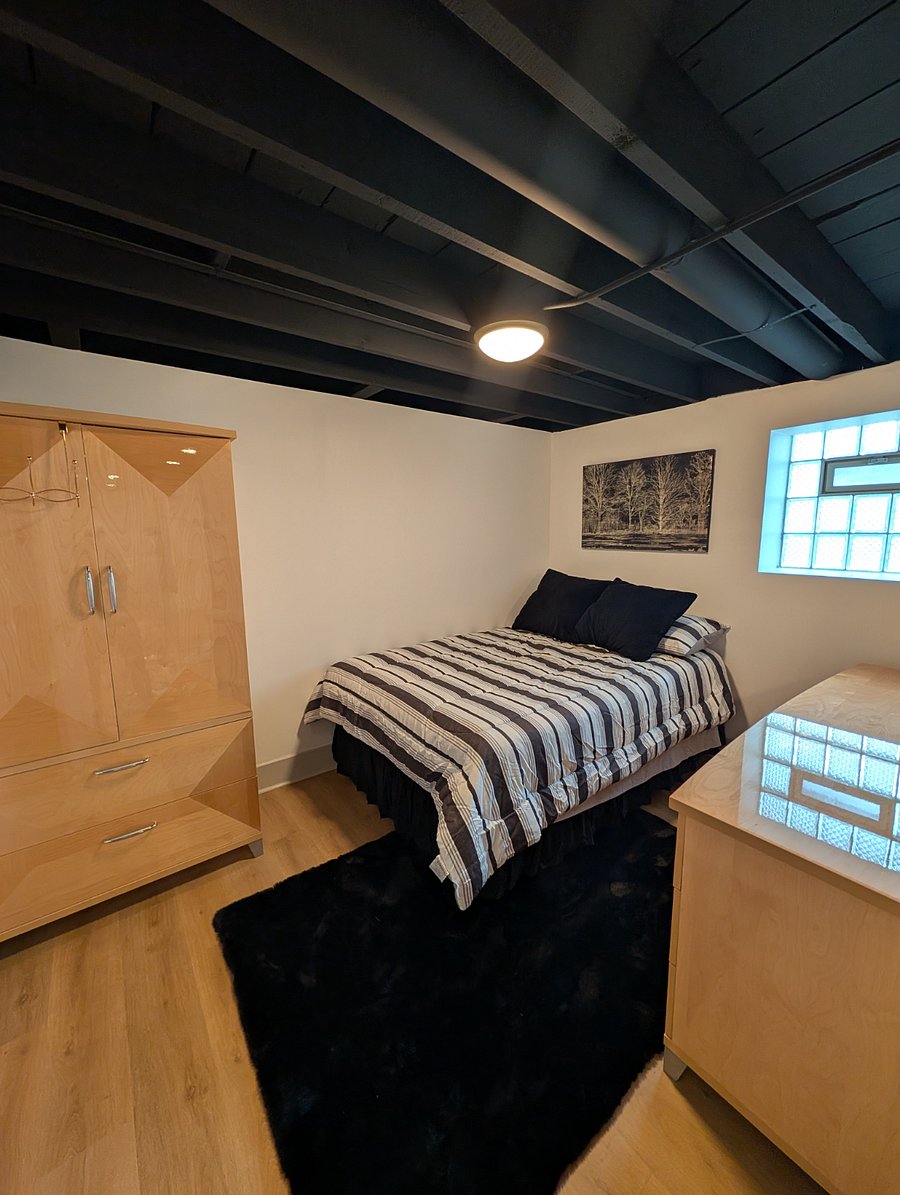 Bedroom with full bed, glass-block windows, and maple dresser with arched mirror.
