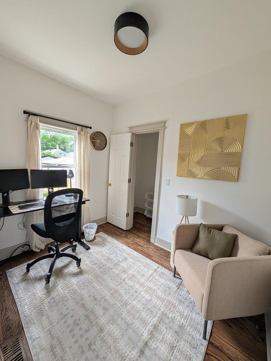 Home office with dual monitors, adjustable standing desk, ergonomic chair, and loveseat.