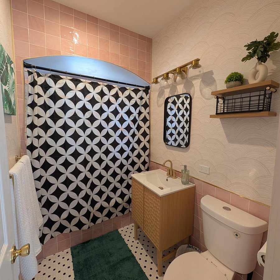 Full bath with blush pink tile, patterned shower curtain, brass globe lighting, and hex-tile floors.
