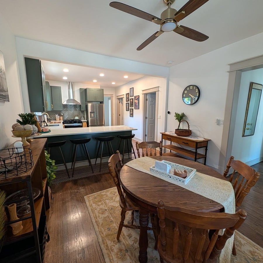 Open-concept dining area with antique oak table, ceiling fan, and quartz breakfast bar adjoining the kitchen.