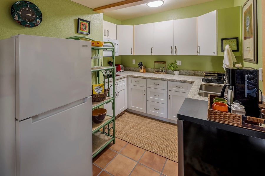 A few steps from the bedroom is a fully renovated galley kitchen set against a fresh sage-green backsplash with southwest accents. A 2-burner induction cooktop, microwave/convection oven with air fryer, 18-inch dishwasher, and 2-well undermount sink make this an efficient, functional space, with crisp white shaker cabinets and granite countertops. A bistro-style bamboo shelving unit provides extra room for cookware and pantry items.