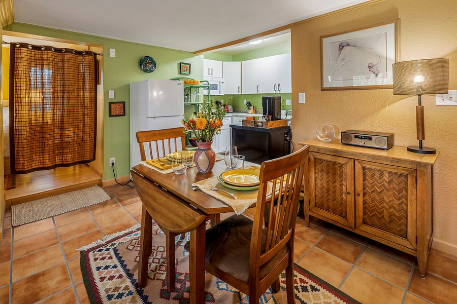Just off the kitchen is a bistro dining table with room for two, set against warm wood paneling, a vintage cabinet, and another kilim rug for old-world charm paired with a retro Bluetooth/CD/radio unit, a smart TV, and Wi-Fi for modern comforts. A bamboo curtain separates the bedroom from the rest of the casita.