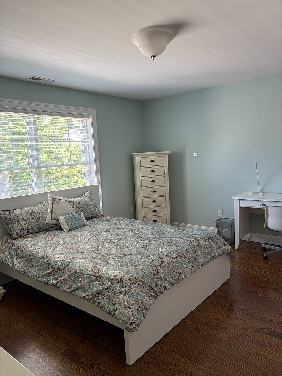 Furnished private bedroom with queen bed, hardwood floors, dresser, and natural light.
