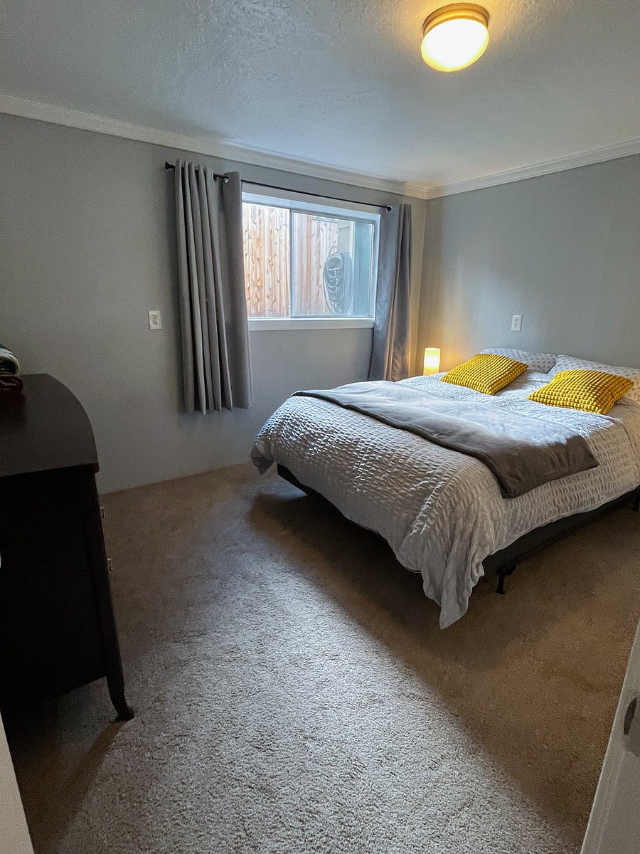 First bedroom with 6 drawer dresser. Window view is fenced walkway with plants.