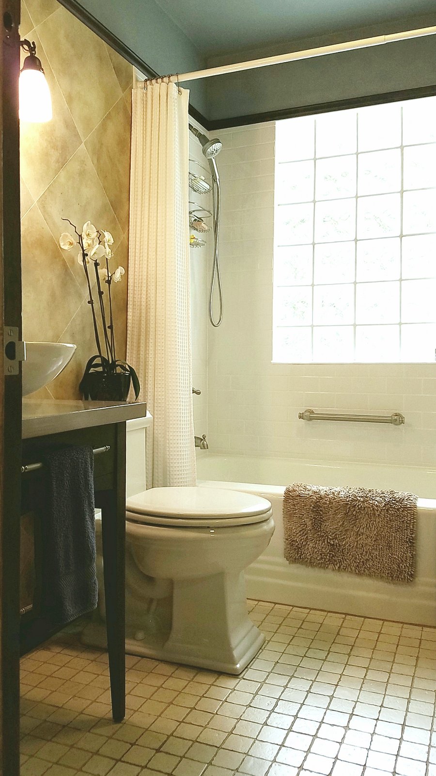 Bathroom with vessel sink, comfort-height Kohler toilet, magnetic handheld shower, grab bars, and glass block window.