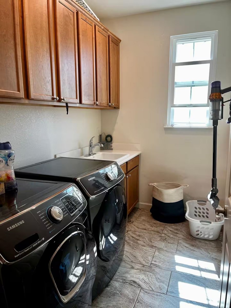 Laundry room equipped with Samsung washer and dryer, a deep utility sink, and wooden cabinetry providing ample storage for clothes and household essentials