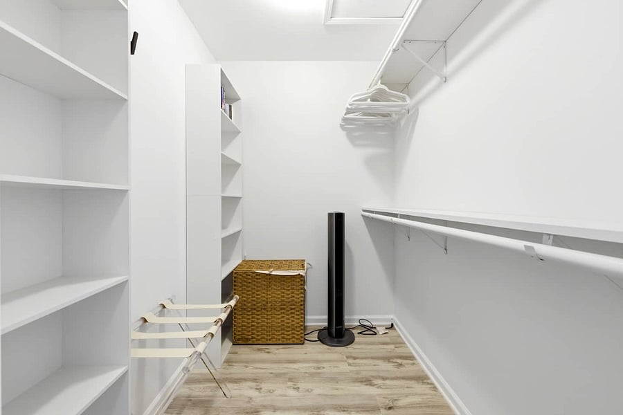 Spacious walk-in closet with built-in shelves, a luggage rack, a hamper, a portable fan, and ample storage.