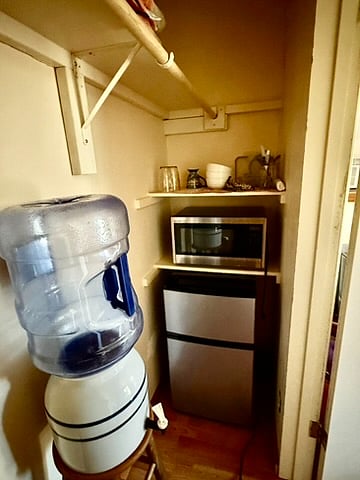 Closet with water carboy, Medium fridge, Microwave and dishes.