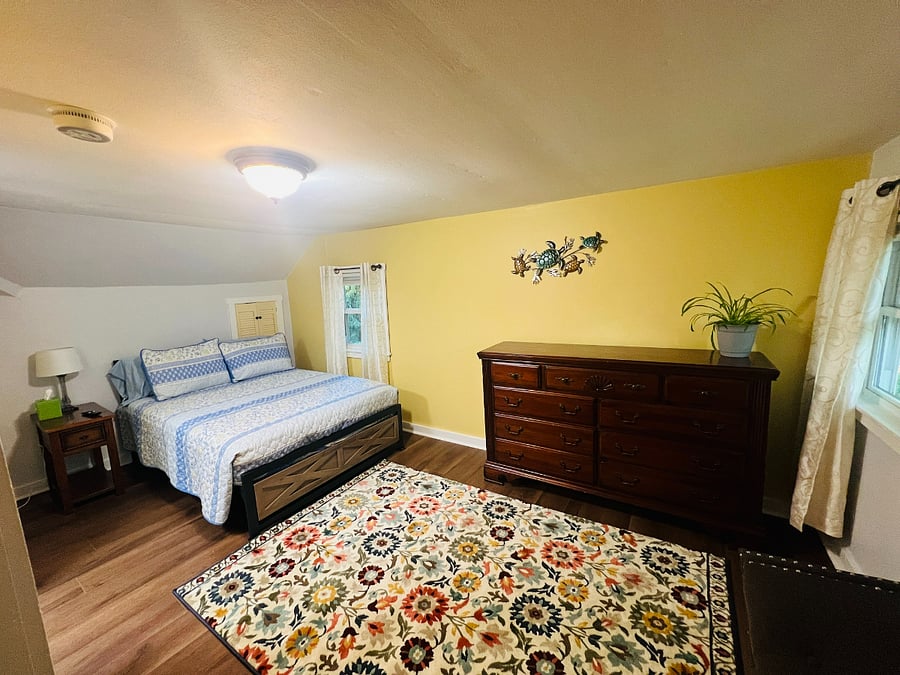 "Sunshine" Bedroom 2nd Floor.  Double bed, large closet, dresser, night stand, TV, AC unit, sitting bench, area rug on hardwood floor