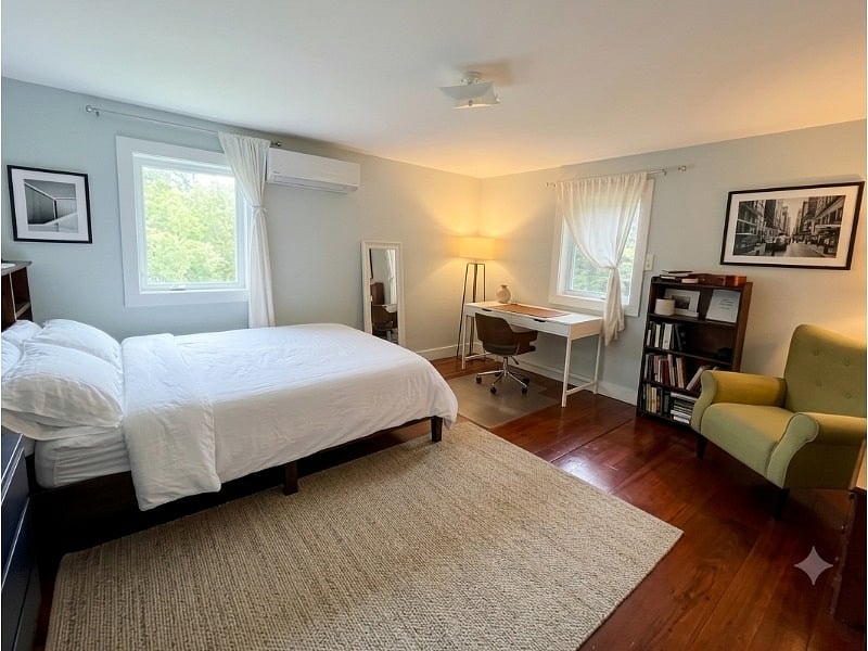 Spacious bedroom furnished with queen size bed, desk, bookcase, armchair, closet, and large dresser.