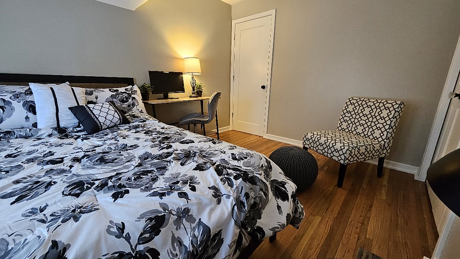 Upstairs front queen bedroom with a dedicated workspace, reading chair, dresser (not pictured), and closet for extended stays.