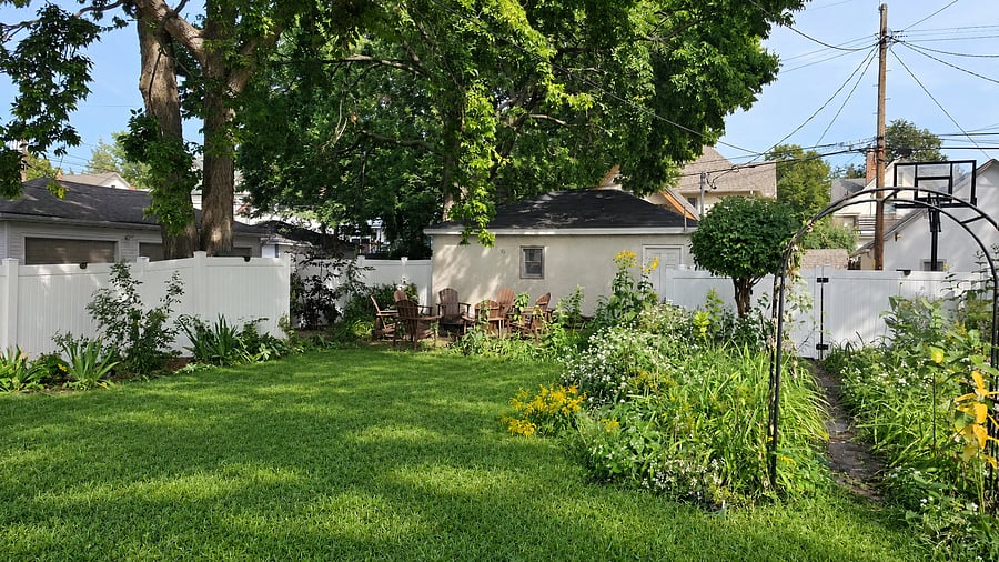 The spacious fenced backyard offers a green lawn framed by mature trees and established gardens, with an Adirondack seating area tucked into the far end of the yard.