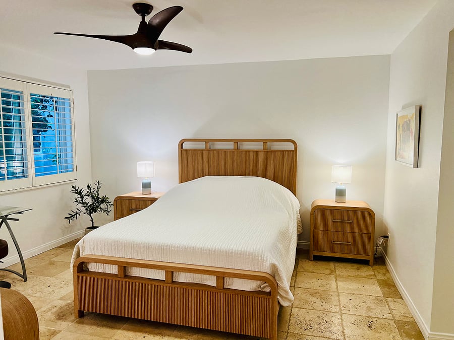Roomy primary bedroom with queen bed, two end-tables, chest of drawers and mirror, glass table for grooming or as a desk overlooking windows