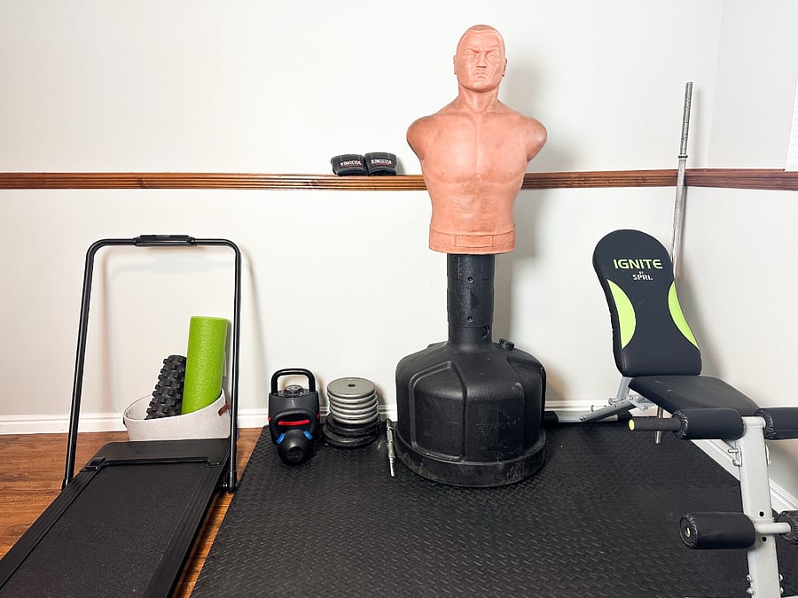 Basement gym with weights, treadmill, "Bob" punching dummy, bench, and kettlebells.