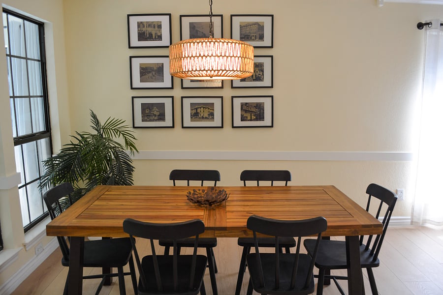 Solid wood dining table comfortably seats 6-8 beneath a statement rattan pendant light. Steel-frame windows with natural light. Gallery wall features vintage photographs of Historic Downtown McKinney just a 10-minute walk away.