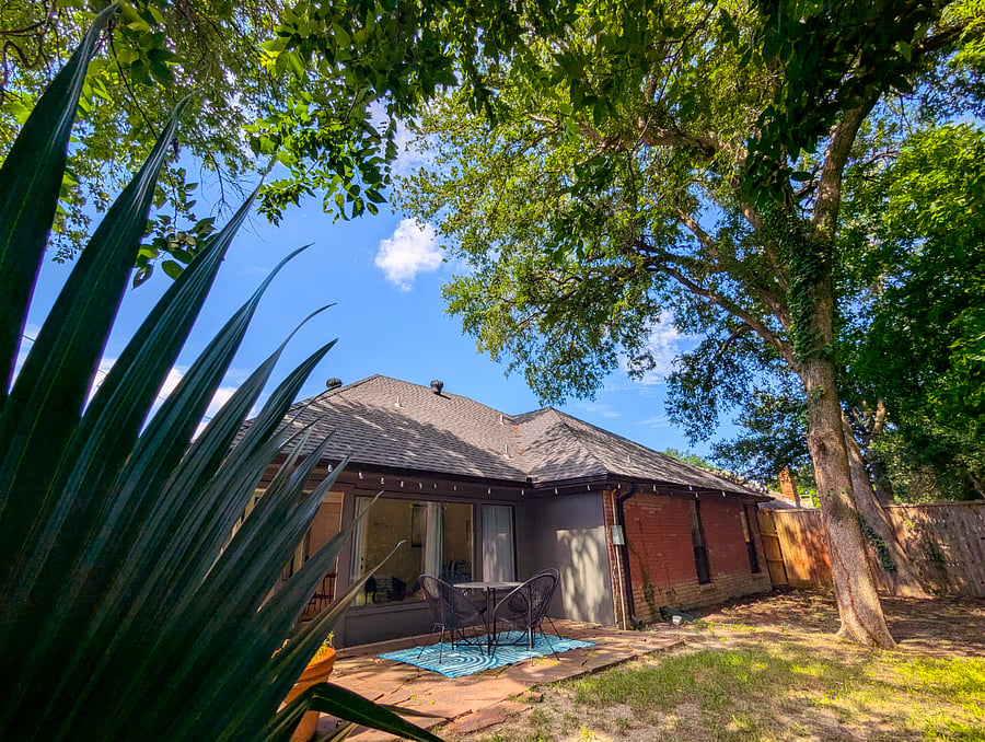 Private fully fenced backyard with mature oak tree canopy, stone patio, and outdoor seating and cafe lighting. Sunroom with large windows visible from yard no rear neighbors. Greenbelt behind property.