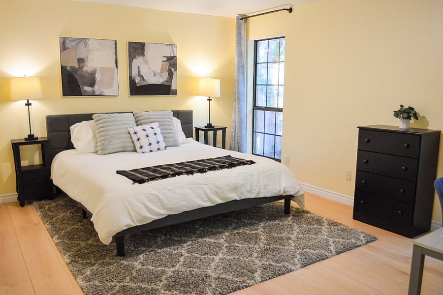 Primary bedroom with king bed, hotel-quality linens, dual nightstands, 5-drawer dresser, and steel-frame window with tree views. Closet provides ample storage for extended stays. Direct access to ensuite spa bathroom.