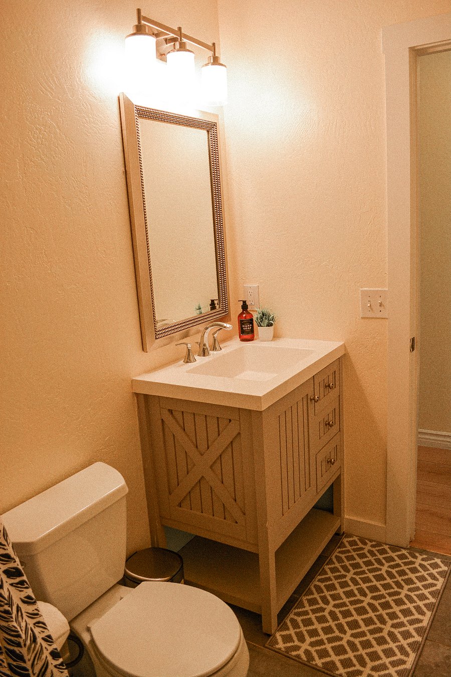 Second full bathroom with farmhouse-style X-panel vanity, quartz countertop, beaded mirror, and warm sconce lighting. Tub/shower combo included. Stocked with hand soap and essentials. Two full bathrooms serve the whole group.