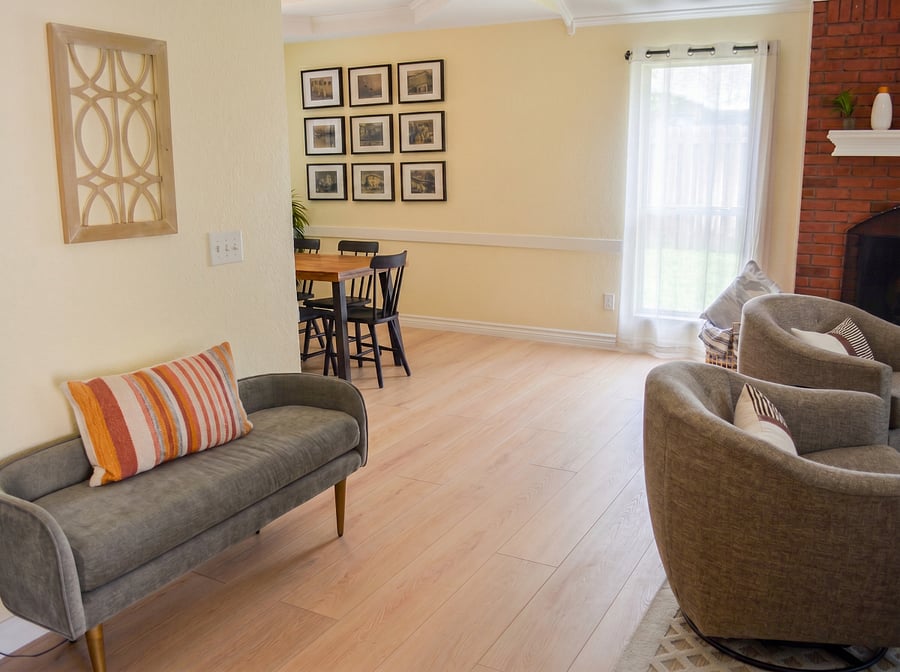 Open-plan layout connecting living and dining areas new luxury vinyl plank flooring throughout, mid-century bench, swivel accent chairs, and brick fireplace visible alongside dining table for 6. Spacious and bright throughout.