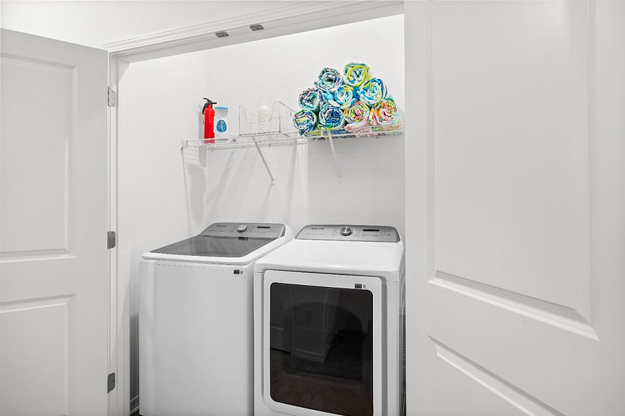 Full size laundry on bedroom floor with fire extinguisher, steamer, and beach towels. 