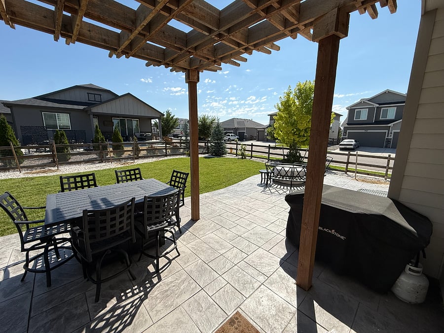 Backyard Oasis: Large 6-person outdoor dining table with built-in gas fire pit; cushions are supplied. Next to a large Blackstone grill. Both are semi-covered by an open concept pergola to allow for shaded, natural light.