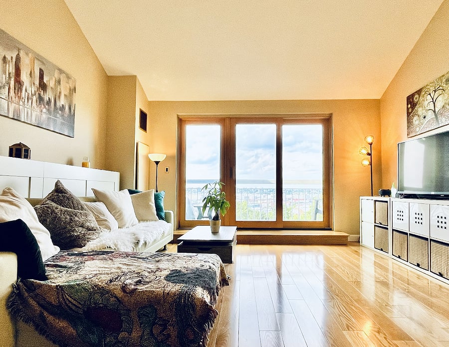 Bright, spacious living room with comfortable furnishings, smart TV, hardwood floors, and expansive windows framing elevated waterfront views.