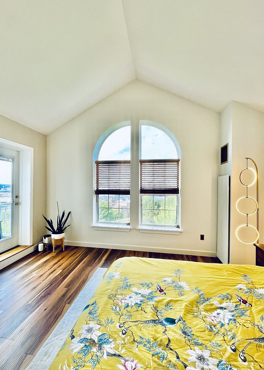 Sun-filled primary bedroom with vaulted ceilings, distinctive arched windows, elevated views, and direct access to the private deck.